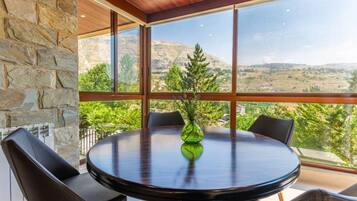 Una mesa redonda con sillas en una habitación con ventanas amplias que dan a un paisaje montañoso.