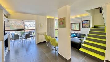 A spacious living area with a staircase, a dining area with chairs, and a view through large windows.