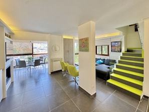 Ein geräumiger Wohnbereich mit Treppe, ein Essbereich mit Stühlen und Blick durch große Fenster.
