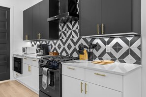 A modern kitchen with black and white patterned backsplash, stainless steel appliances, and gold handles on cabinets. - 10 Min to Broadway-Rooftop Hangout-Garage Parking (Nashville)