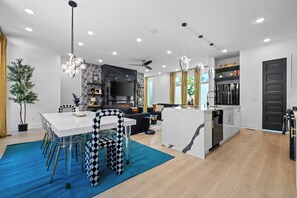A modern kitchen with a central island, a dining area with a checkered chair, and a living space with a sofa and a TV. - 10 Min to Broadway-Rooftop Hangout-Garage Parking (Nashville)