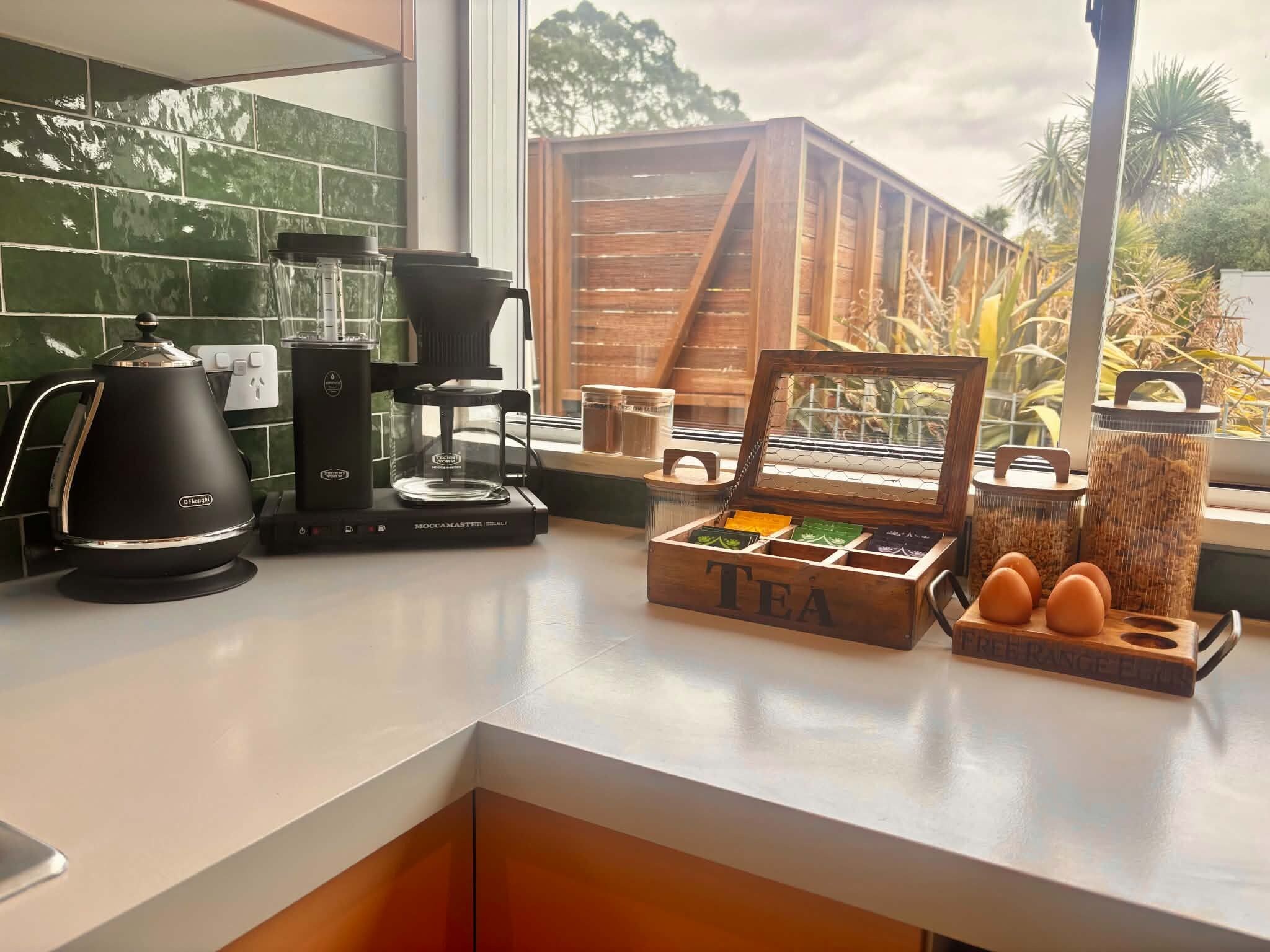 Una encimera de cocina con cafetera, caja de té y un soporte de madera para huevos.