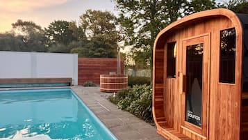 Estructura de sauna de madera junto a una piscina, con cielo despejado al fondo.