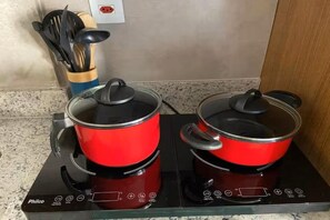 Two red pots on a black induction cooktop with a wooden utensil holder and a wall socket. - New Listing (São Paulo)