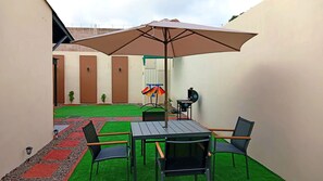 Eine Terrasse mit Tisch, Stühlen, einem Grill und einem großen Sonnenschirm.