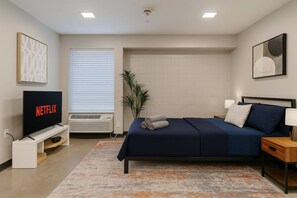 A modern bedroom with a bed, a TV, a plant, and a window with blinds. - Charming Studio in Historic Five Points South #90 (Birmingham)