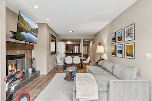 A modern living room with a fireplace, a television mounted on the wall, a dining area with a table and chairs, and a sofa. - Ski condo on Eagle River,  Close to BC & Vail (Avon)