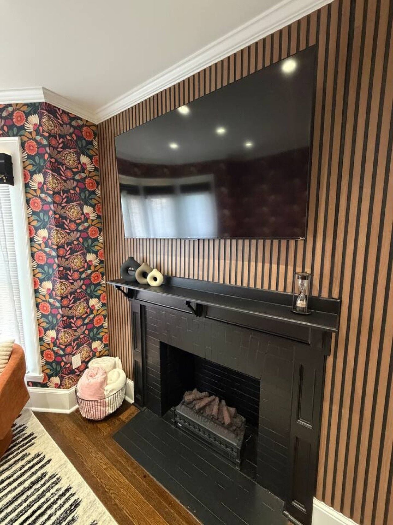 A modern living room with a fireplace, a flat-screen TV mounted above it, and a patterned wallpaper on the adjacent wall.