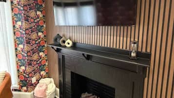 A modern living room with a fireplace, a flat-screen TV mounted above it, and a patterned wallpaper on the adjacent wall.