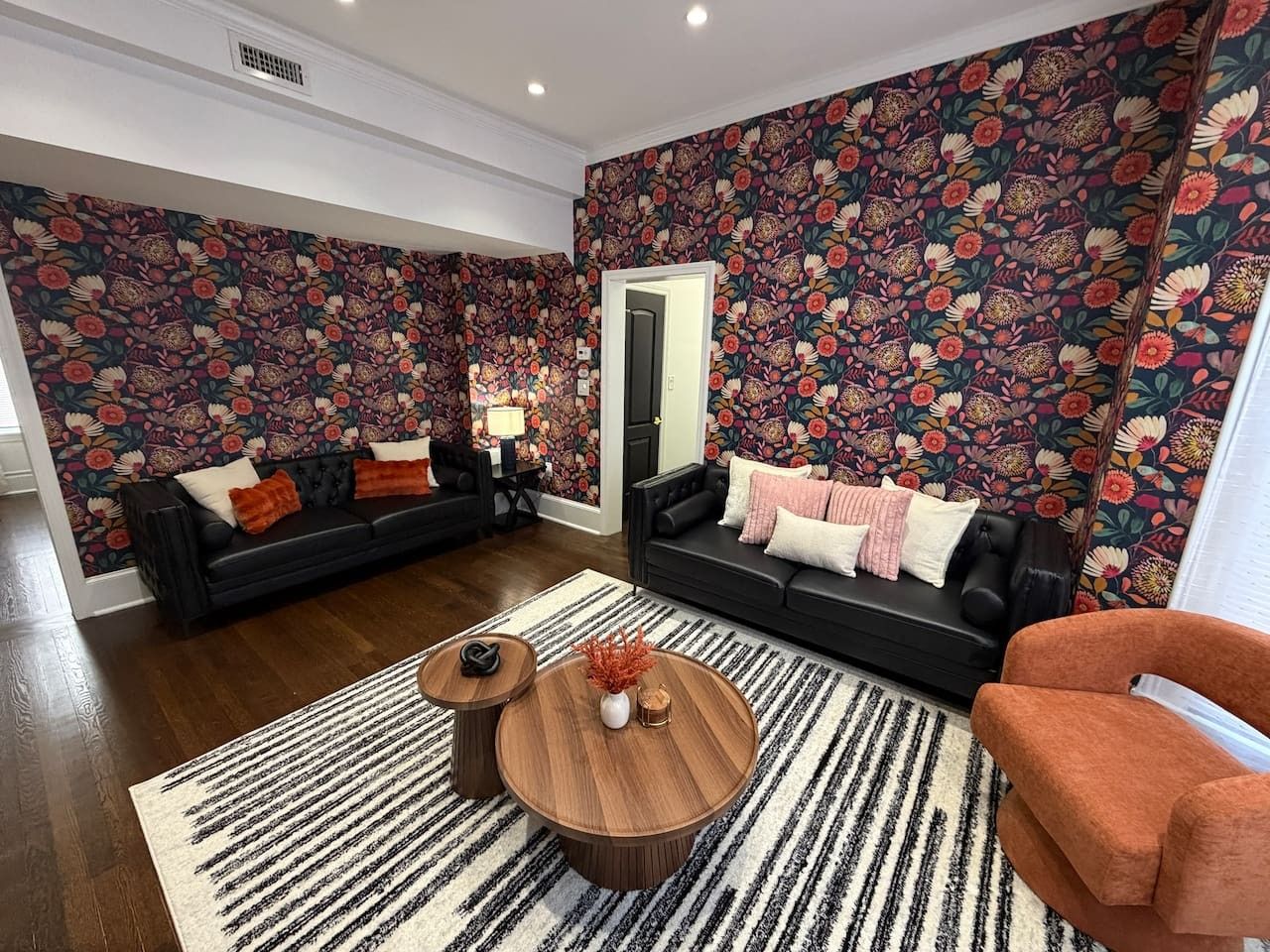 A living room with two black sofas, a round coffee table, and a patterned wall.