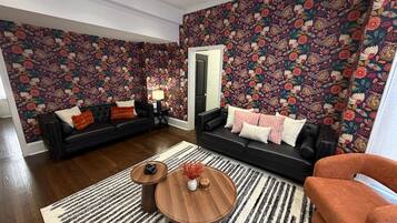 A living room with two black sofas, a round coffee table, and a patterned wall.