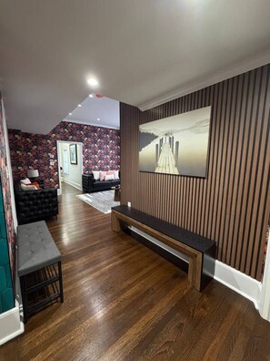 A modern living room with a wooden floor, a black sofa, a bench, and a large painting on the wall. - The Mount Vernon Retreat with private yard (Lowell)
