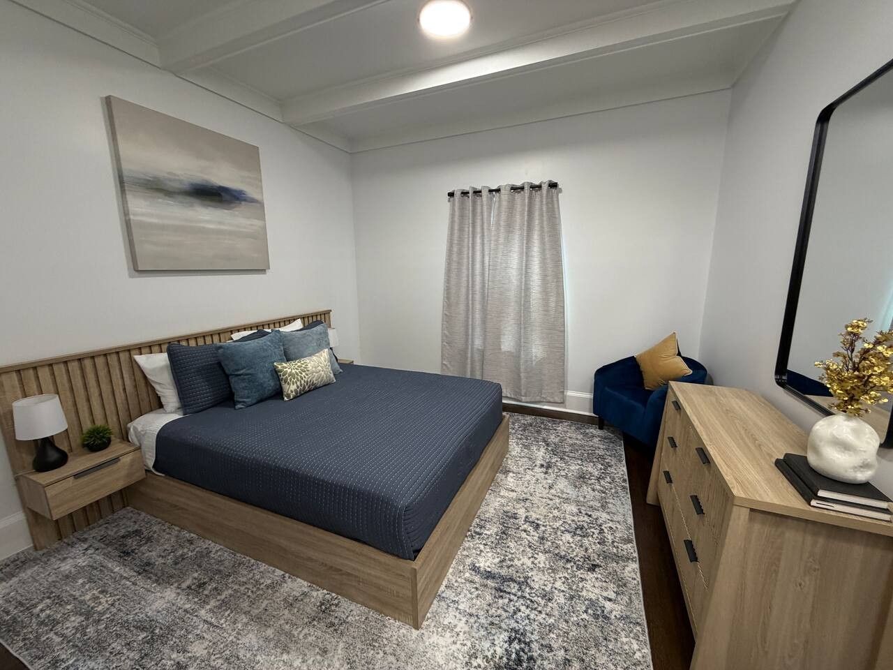 Ett modernt sovrum med en stor säng, sängbord, en byrå, en spegel och ett fönster med gardiner.