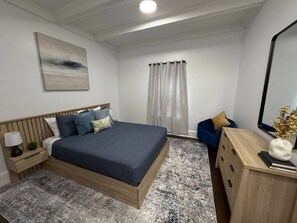 Ein modernes Schlafzimmer mit einem großen Bett, Nachttischen, einer Kommode, einem Spiegel und einem Fenster mit Vorhängen.