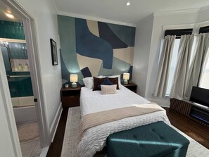 A bedroom with a bed, nightstands, a TV, and a bathroom with a shower and toilet. - The Mount Vernon Retreat with private yard (Lowell)