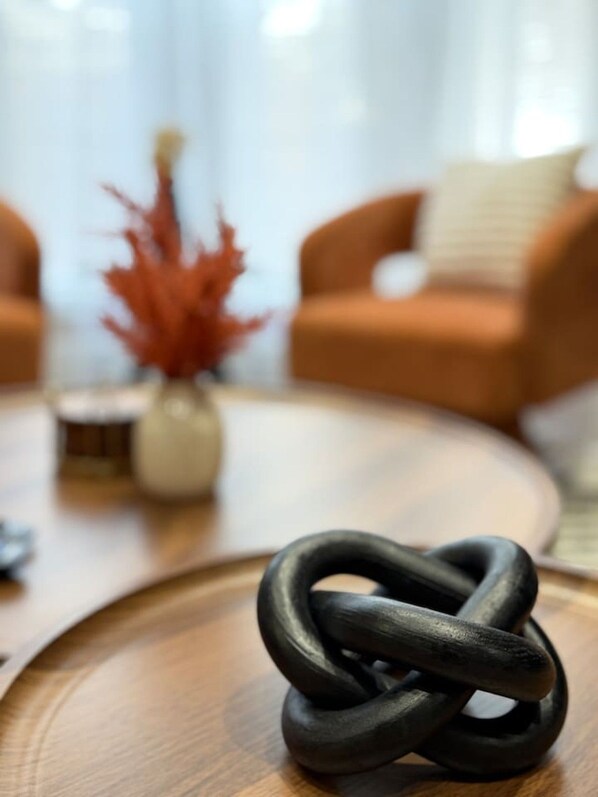 A black interwoven object on a wooden surface, with a blurred background featuring a sofa and a vase with red foliage. - The Mount Vernon Retreat with private yard (Lowell)