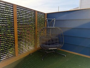 Ein Hängekorbsessel in einer Ecke mit einem grünen Rasenteppichboden und einer vertikalen Gartenwand.