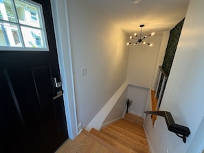 A staircase with wooden steps, a black door, and a ceiling light fixture. - Modern Studio Suite -Private Entrance -W/D and A/C (Lowell)