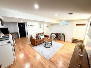 A modern living space with a wooden floor, a sofa, a coffee table, and a dining area with chairs. - Modern Studio Suite -Private Entrance -W/D and A/C (Lowell)