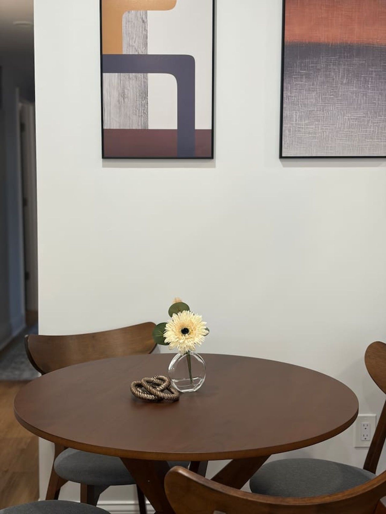 Una mesa redonda de comedor con un florero y un adorno de cuerda enrollada.