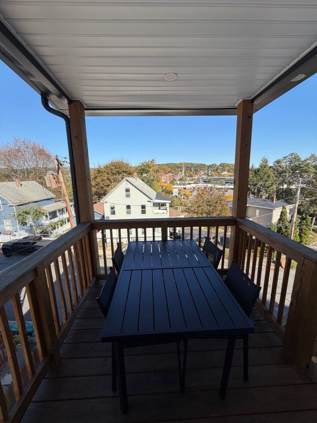Un espacio al aire libre techado con una mesa y sillas, con vista a un barrio residencial.
