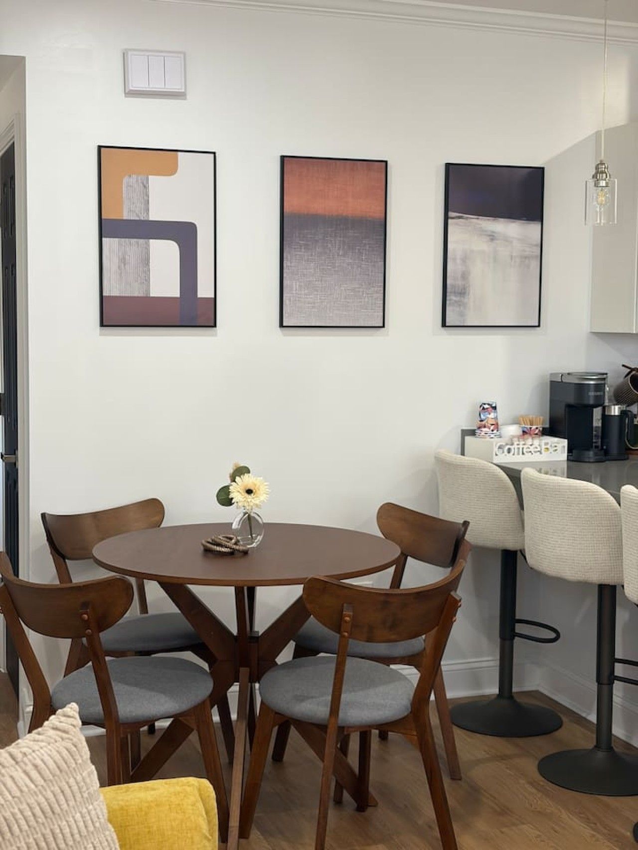 Un comedor con una mesa redonda, cuatro sillas y tres cuadros abstractos en la pared.
