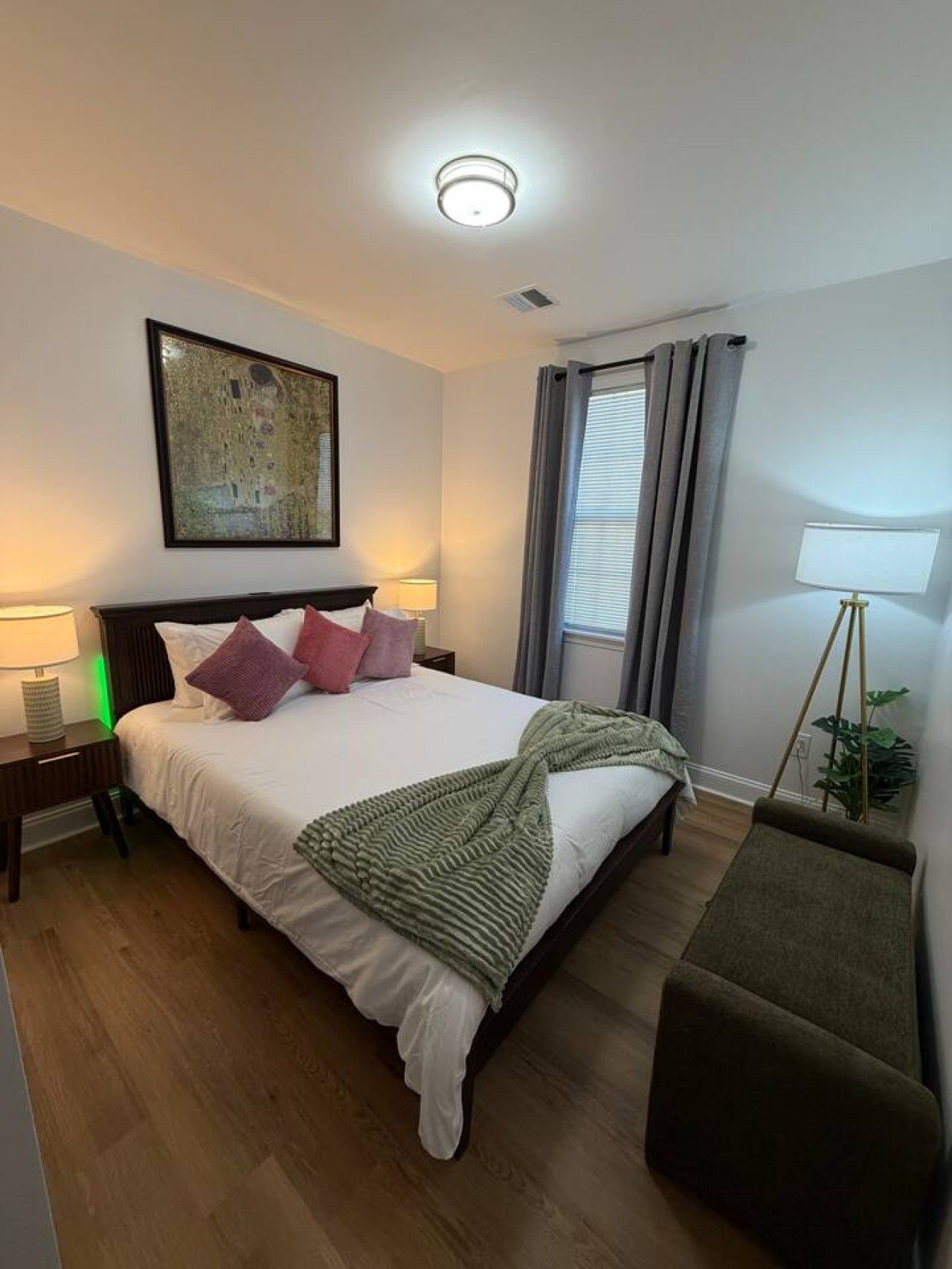 Habitación de hotel con cama, lámparas de noche, un cuadro, una ventana con cortinas y una lámpara de pie.