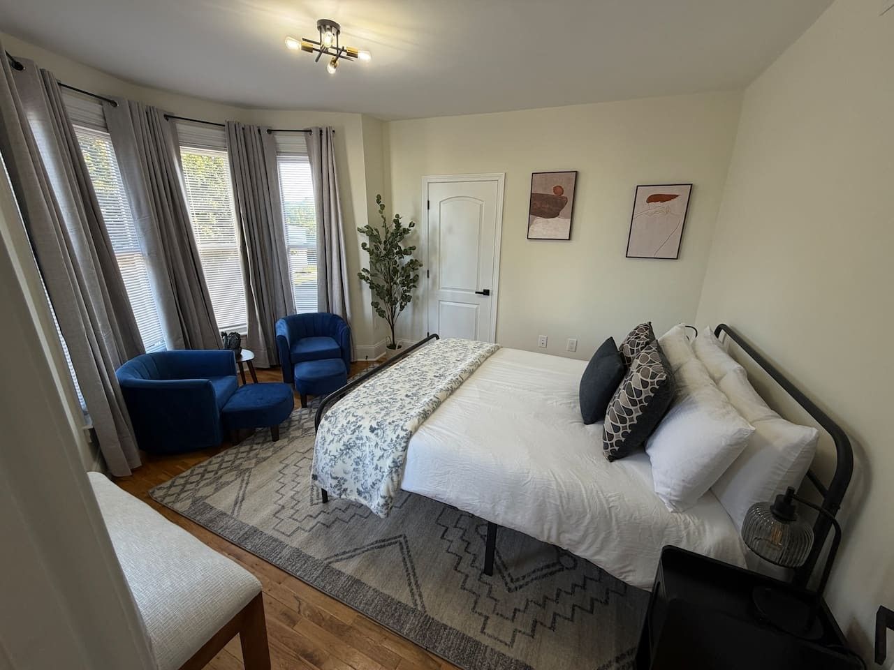 Une chambre à coucher avec un lit, deux chaises bleues, une table de chevet, une lampe et une porte.