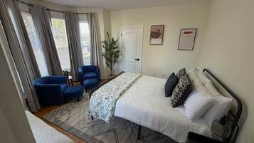 Une chambre à coucher avec un lit, deux chaises bleues, une table de chevet, une lampe et une porte.