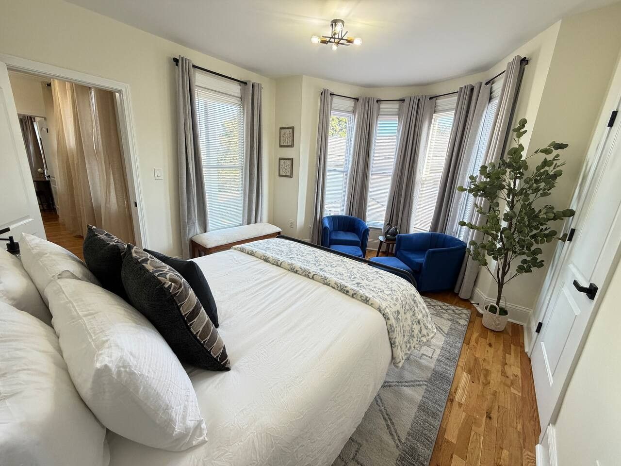 A bedroom with a large bed, a sitting area with blue chairs, and a potted plant.
