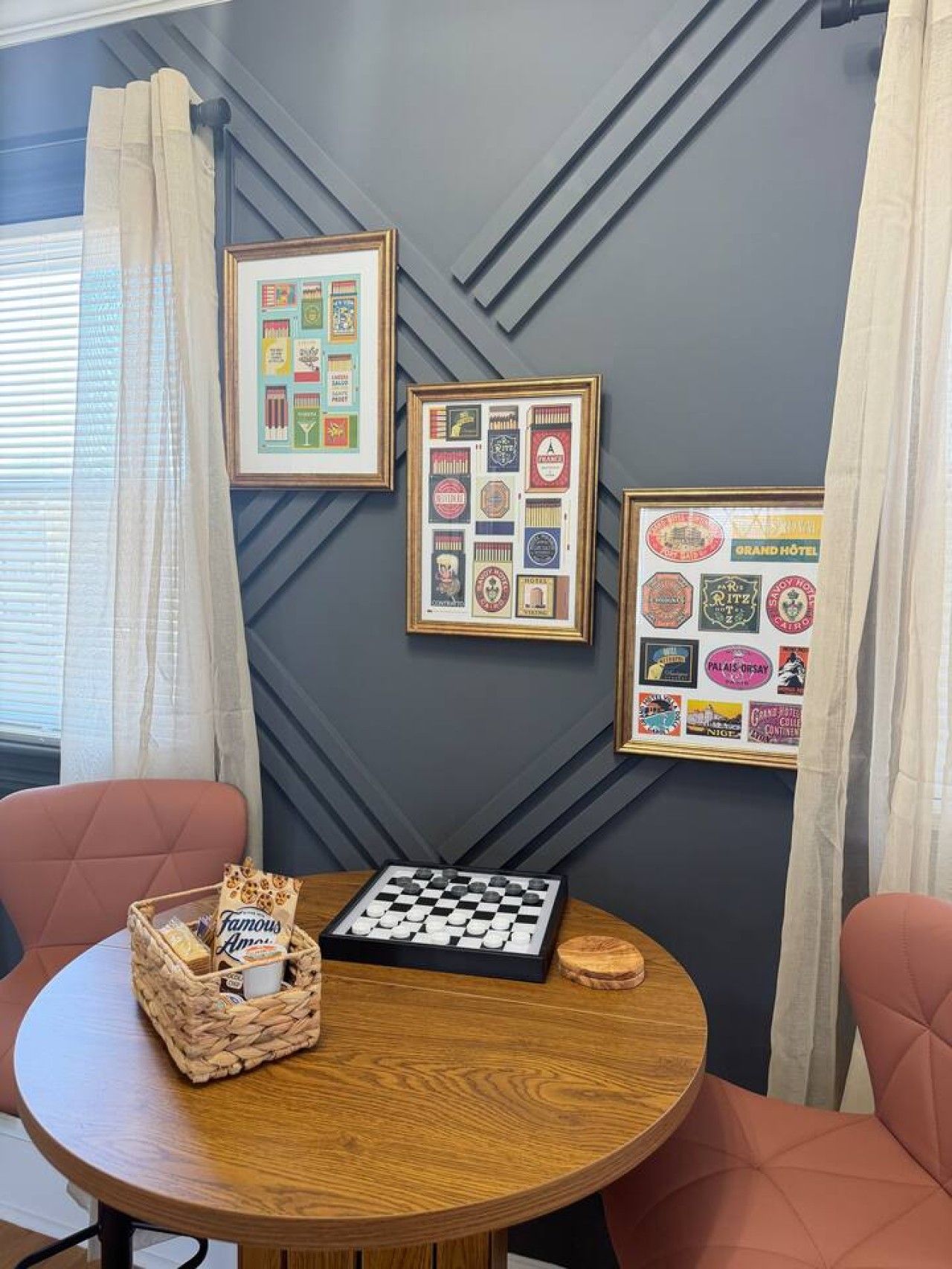 A room with a round wooden table, two chairs, a chessboard, and framed wall decorations.