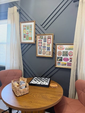 Una habitación con una mesa redonda de madera, dos sillas, un tablero de ajedrez y adornos enmarcados en la pared.