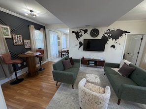 Una sala de estar con un sofá verde, un sillón estampado, una mesa de centro de madera y un mapa mundial en la pared.