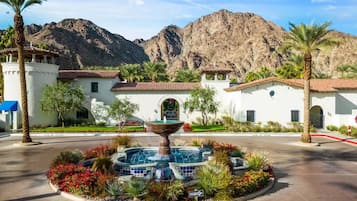 A courtyard with a fountain, palm trees, and a building with a tiled roof.