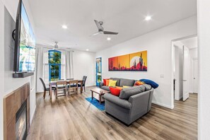 A modern living room with a fireplace, a dining area, and a large window with blue curtains. - Modern King 1BR/1BA Legacy Villa Near Main Pool (A) (La Quinta)