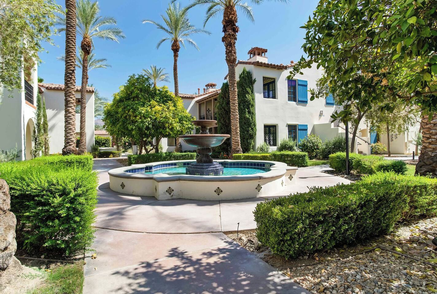 A courtyard with a fountain, palm trees, and a building with blue shutters.