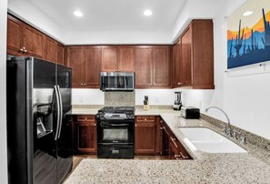 A kitchen with wooden cabinets, a stainless steel refrigerator, a microwave, a stove, a sink, and a painting on the wall. - Modern King 1BR/1BA Legacy Villa Near Main Pool (A) (La Quinta)