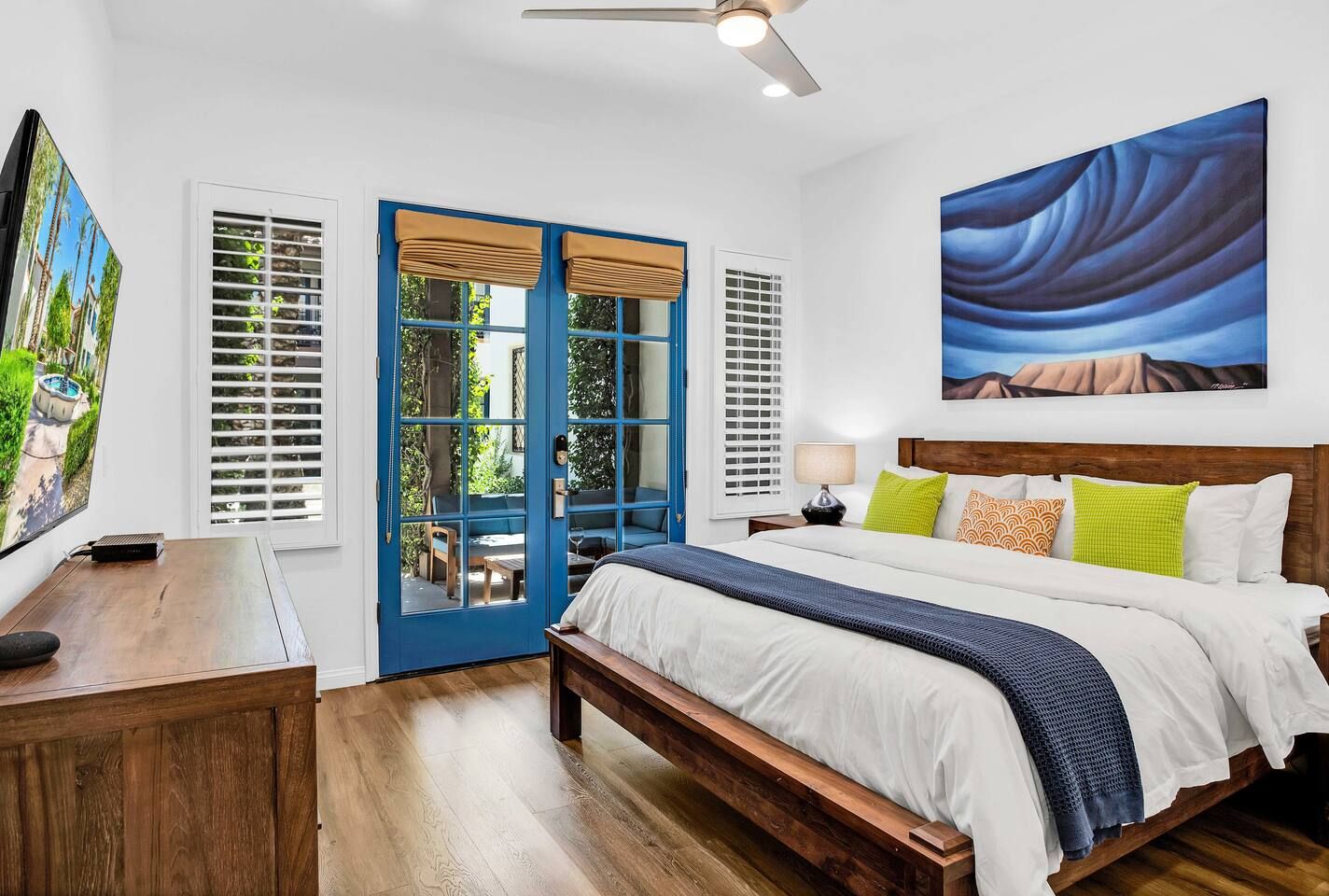 A bedroom with a bed, a desk, a TV, and a painting.