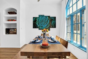Een eetgedeelte met een houten tafel, blauwe placemats en een vaas met bloemen.