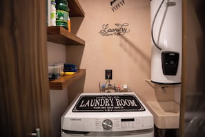 Ein kleiner Hauswirtschaftsraum mit einer Samsung Waschmaschine, einem Warmwasserbereiter und einem Regal mit Reinigungsmitteln.