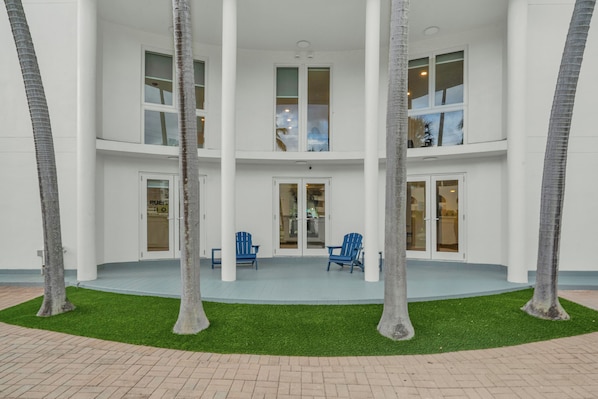 Un edificio de varios pisos con un patio central, dos sillas azules y palmeras.