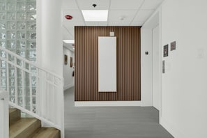 Un interior moderno con un panel de madera, una escalera con barandillas de vidrio y un pasillo con piso de baldosas.