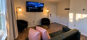 A modern living room with a flat-screen TV mounted on the wall, two armchairs, a sofa, and a small round table. - Evermore Residence • Private Home • Sleeps 3 (Roanoke)
