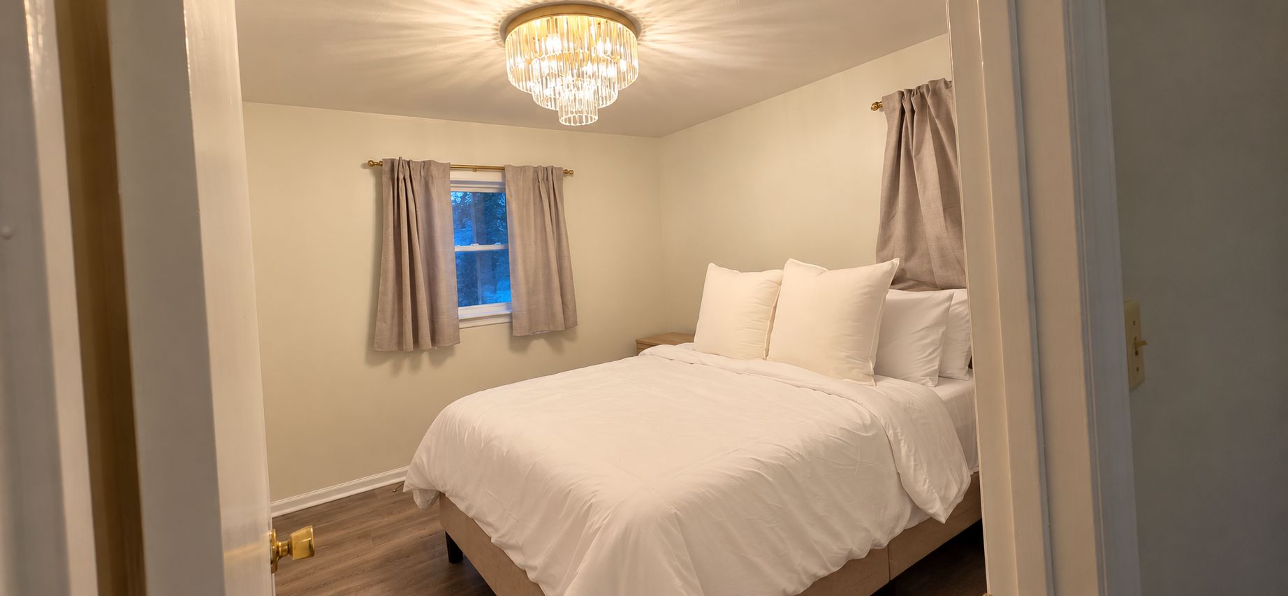 A bedroom with a bed, curtains, a chandelier, and a window.