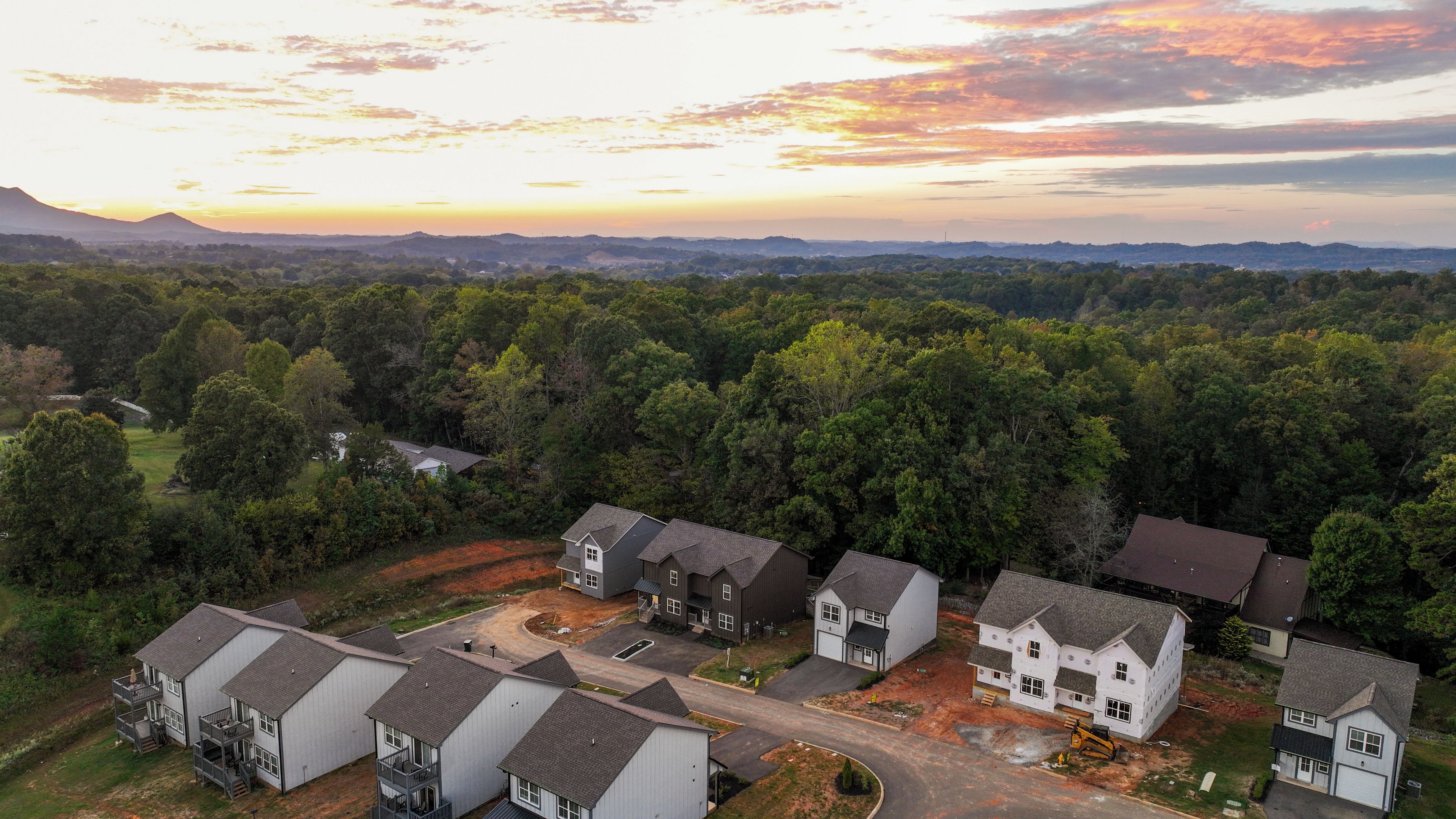 A residential area with multiple houses, a clear sky, and a distant mountain range.