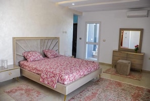 Ein Schlafzimmer mit Bett, Nachttisch, Kommode, Spiegel und einer Tür zu einem anderen Raum.