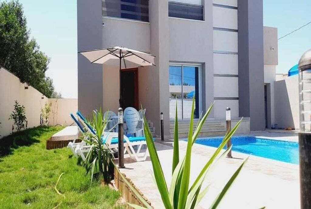A modern building with a swimming pool, outdoor seating, and a well-maintained lawn.