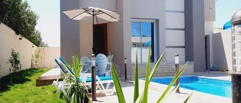 A modern building with a swimming pool, outdoor seating, and a well-maintained lawn.
