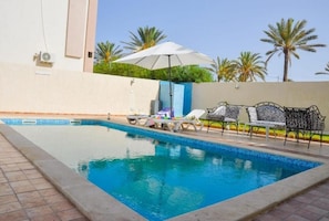 Ein Swimmingpool mit Liegestühlen und Sonnenschirmen, umgeben von Palmen.