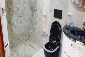 Ein Badezimmer mit Duschkabine aus Glas, einer schwarzen Toilette und einem Waschbecken mit schwarzer Arbeitsplatte.
